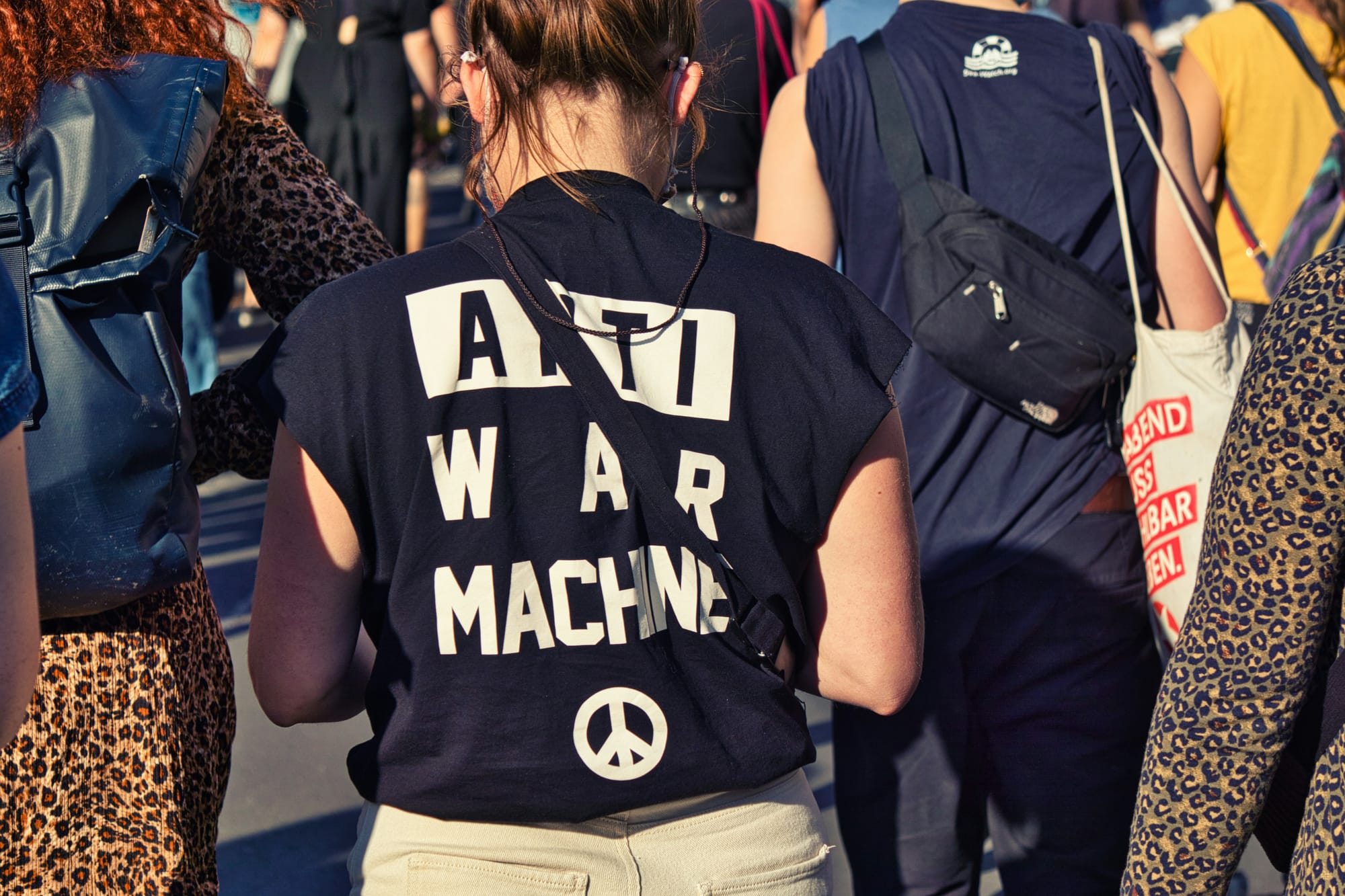여러 사람의 뒷모습. 그 중 한 명의 옷 뒷면에 "ANTI WAR MACHINE"이라고 쓰여 있다.